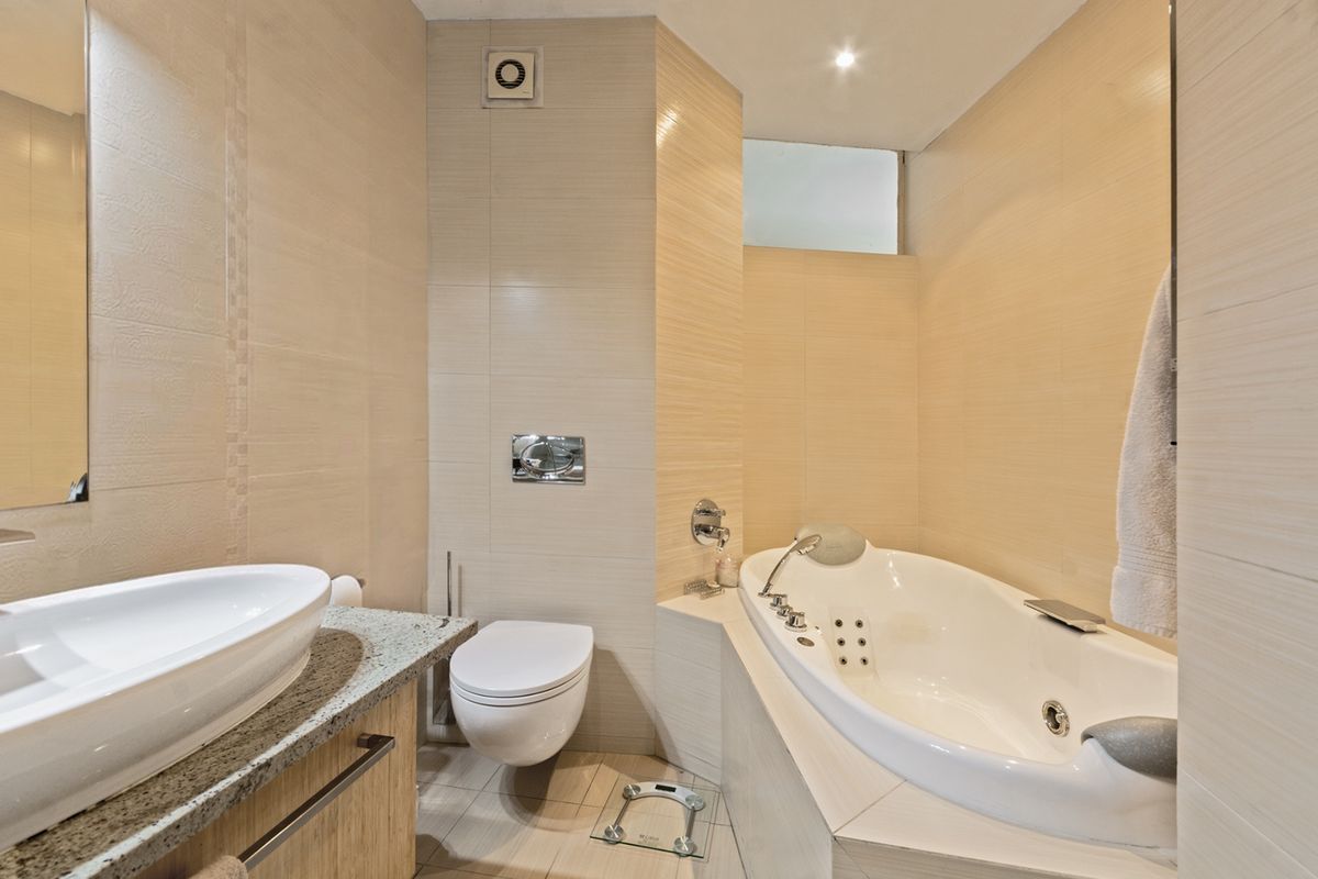 Modern bathroom featuring a wall-mounted toilet, a built-in jetted bathtub, and a vanity with a stone countertop and vessel sink.