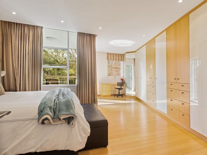 Spacious bedroom featuring extensive built-in cabinetry, a dedicated desk area, laminate flooring, and large windows with natural light.