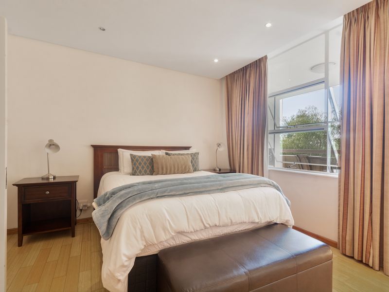 A well-maintained bedroom featuring laminate flooring, recessed lighting, and a large awning window with integrated curtain tracks.