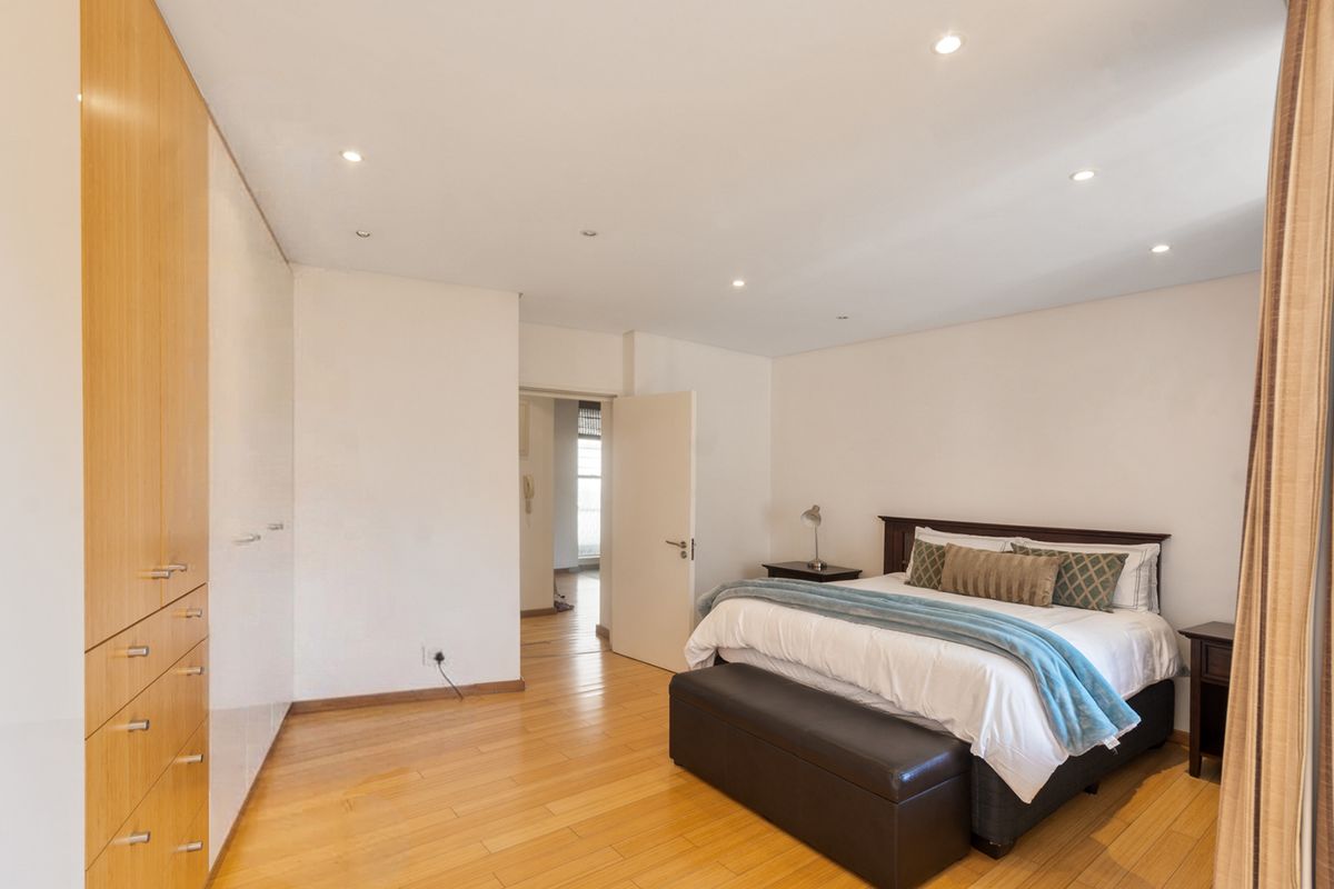 Spacious bedroom featuring light timber flooring, extensive built-in cabinetry, and recessed ceiling lighting, offering a clean and well-maintained living space.
