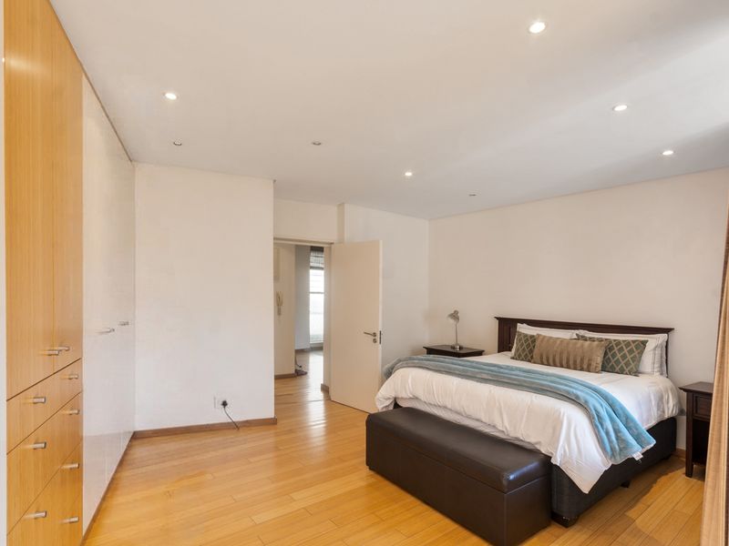 Spacious bedroom featuring light timber flooring, extensive built-in cabinetry, and recessed ceiling lighting, offering a clean and well-maintained living space.
