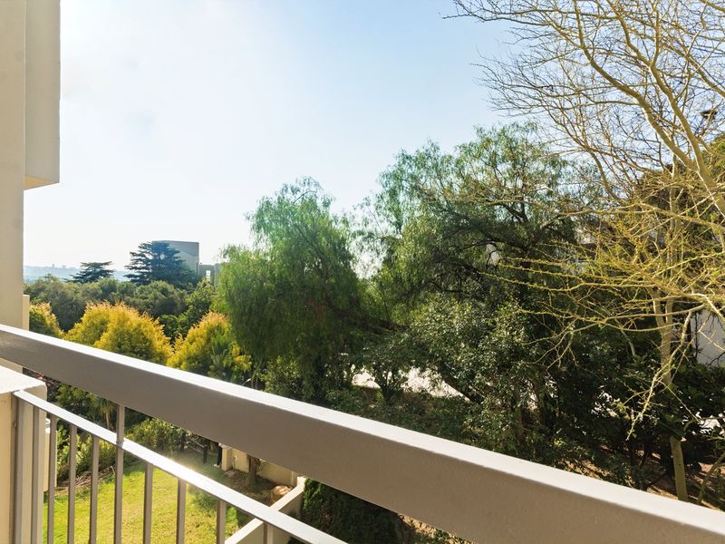 A private balcony featuring a metal railing with a pleasant view of the surrounding trees and greenery.