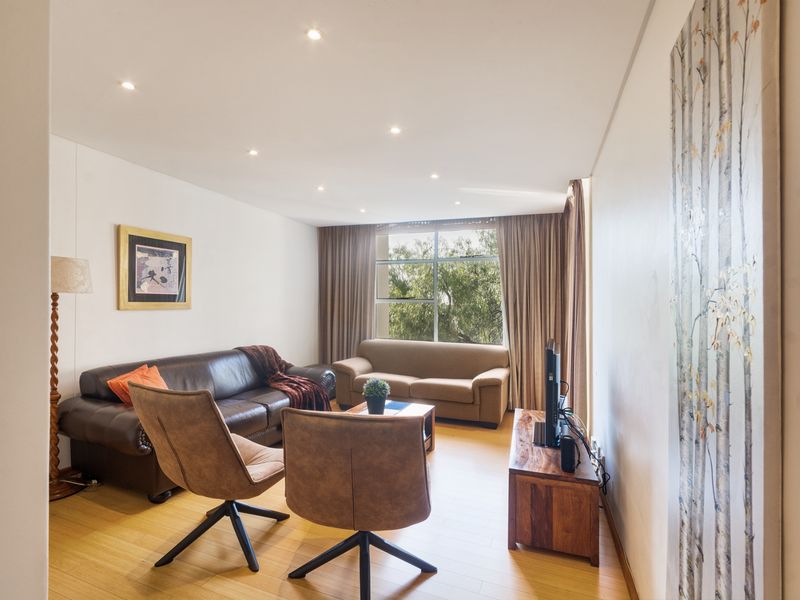 A bright and well-maintained living room featuring laminate flooring, recessed downlighting, and a large window providing natural light.