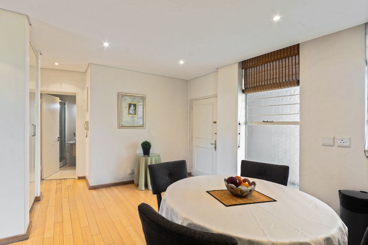 A bright living area featuring timber flooring, recessed downlighting, and a window with a bamboo roller blind, providing a clean and functional space.