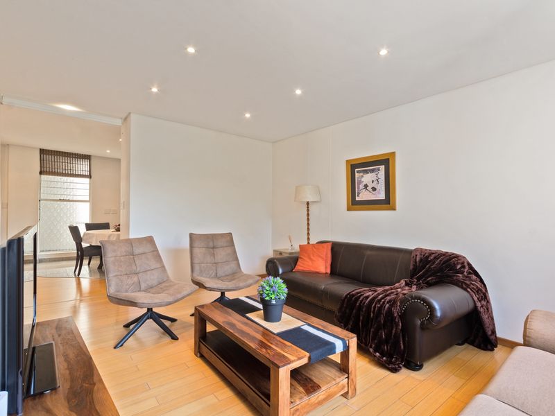 A bright and well-maintained living room featuring recessed downlighting and light-toned laminate flooring, with an open-plan flow leading to the dining area.