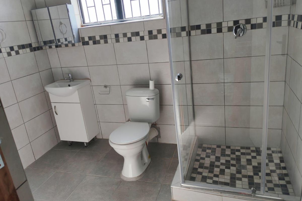 A clean, functional bathroom featuring a glass shower enclosure, vanity basin, and toilet with neutral wall and floor tiling.