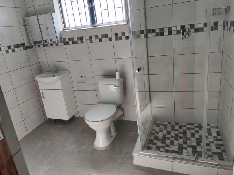 A clean, functional bathroom featuring a glass shower enclosure, vanity basin, and toilet with neutral wall and floor tiling.
