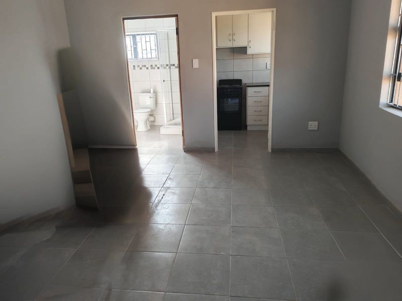 Open plan living area with neutral tiled flooring, leading into a functional kitchen and a separate bathroom with a shower.