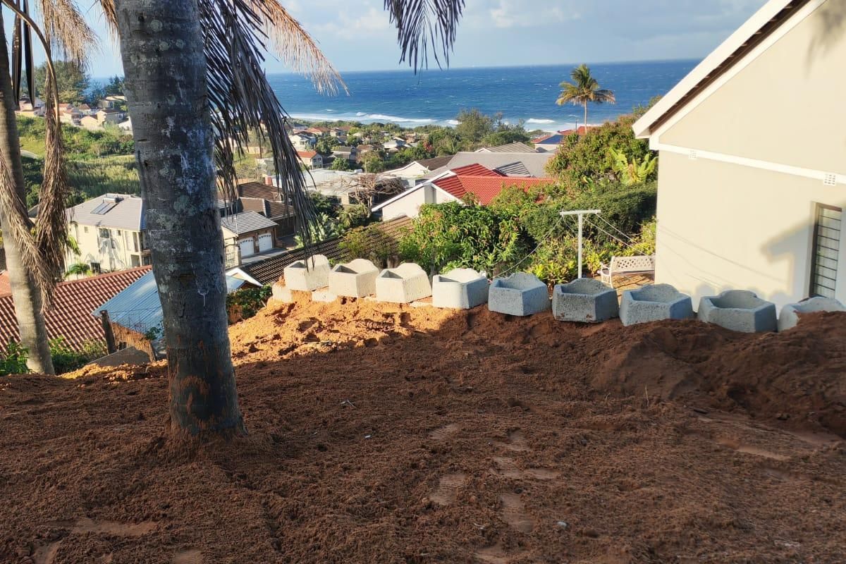 Rear exterior view of the property featuring a sloped, unlandscaped yard with retaining wall blocks and a scenic coastal ocean view.
