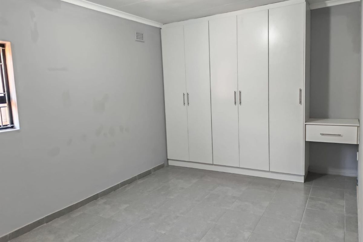 A clean, empty bedroom featuring neutral tiled flooring, built-in white wardrobes, and an integrated vanity unit, ready for personalization.