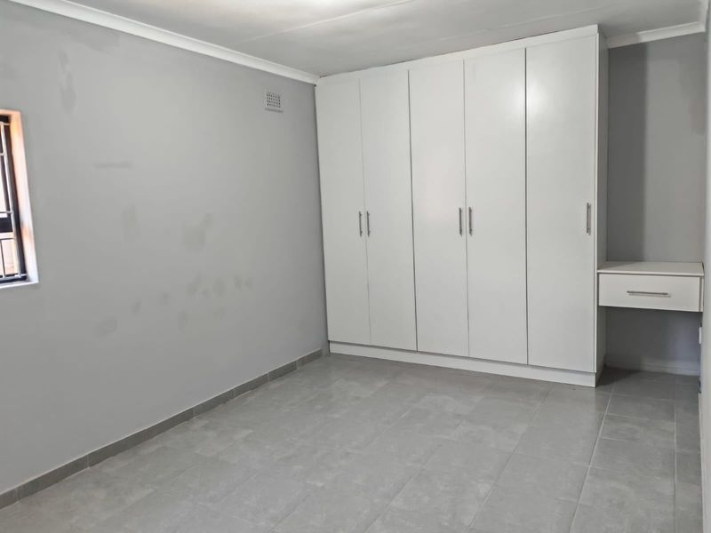 A clean, empty bedroom featuring neutral tiled flooring, built-in white wardrobes, and an integrated vanity unit, ready for personalization.