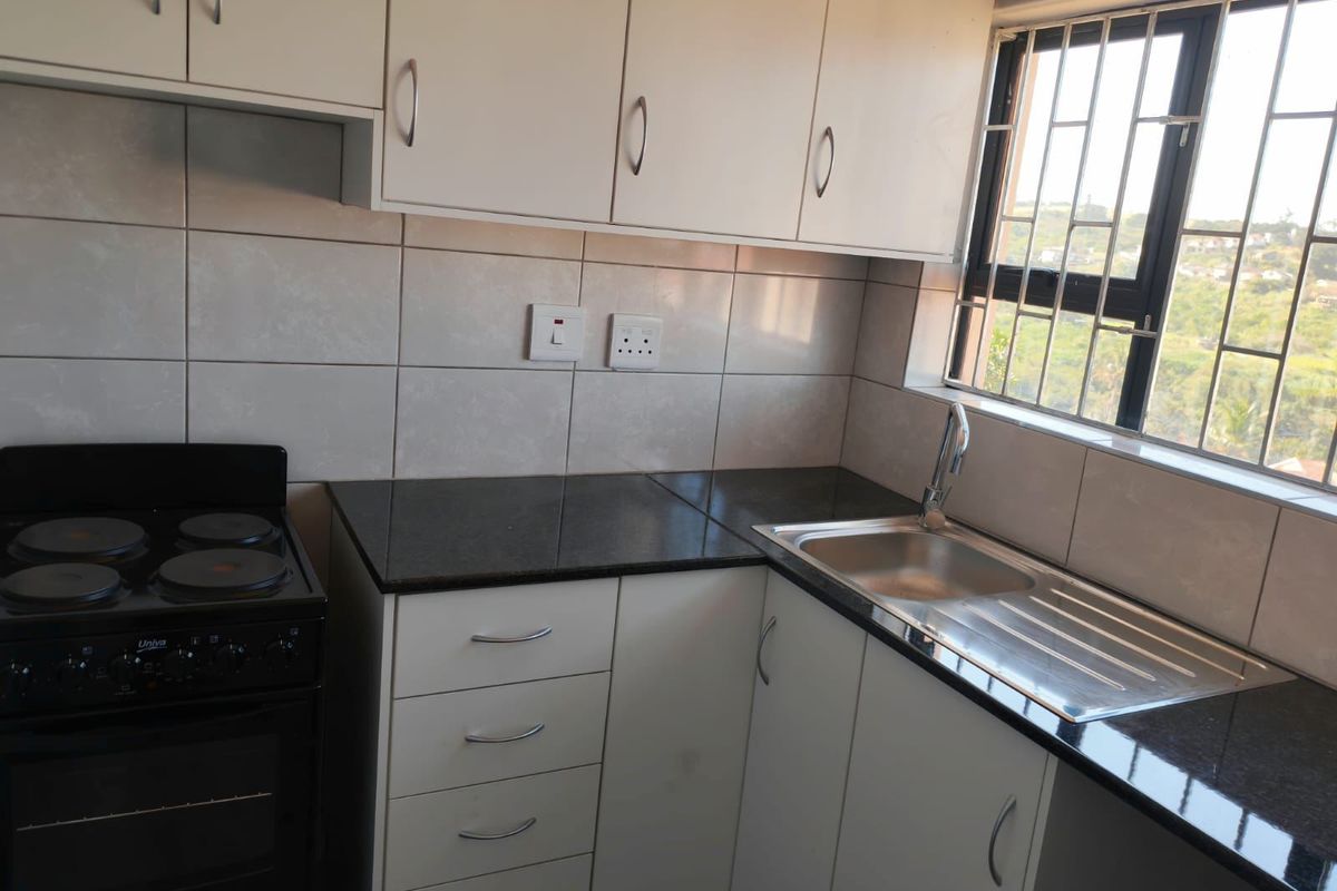 A compact, functional kitchen featuring white cabinetry, dark granite countertops, a stainless steel sink, and a freestanding stove with a tiled backsplash.