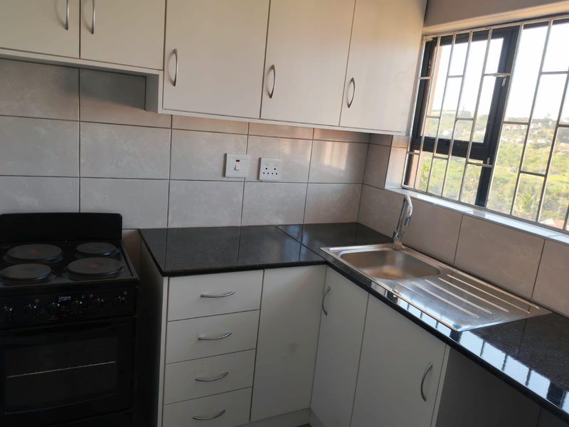 A compact, functional kitchen featuring white cabinetry, dark granite countertops, a stainless steel sink, and a freestanding stove with a tiled backsplash.