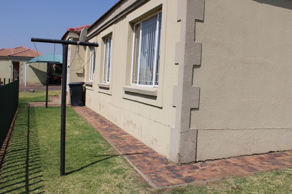 Rear exterior view of the townhouse featuring plastered walls, brick paving, and security bars on the windows.