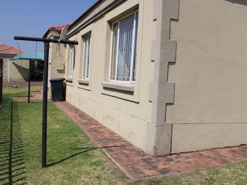 Rear exterior view of the townhouse featuring plastered walls, brick paving, and security bars on the windows.