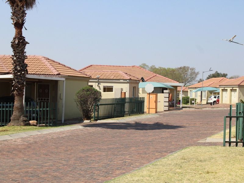A view of a residential townhouse complex street featuring paved driveways, carports, and tiled roof structures.