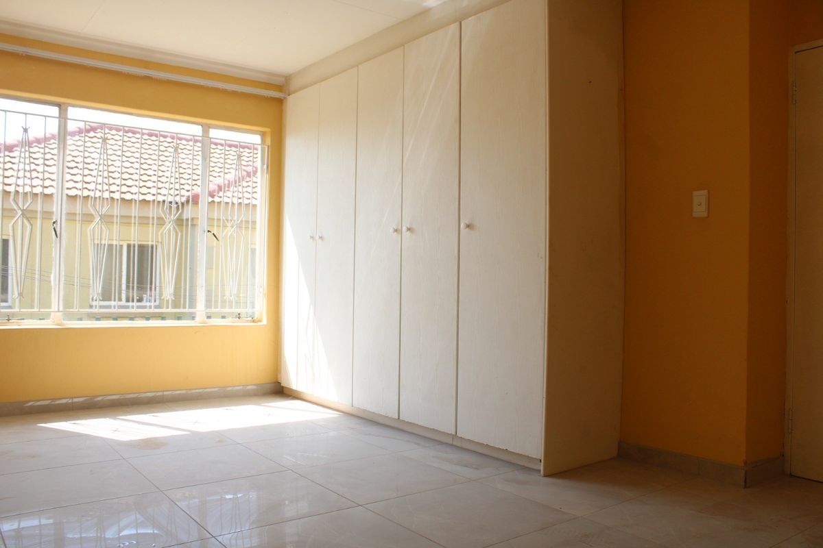 A vacant bedroom featuring built-in cupboards, tiled flooring, and a window fitted with security bars.