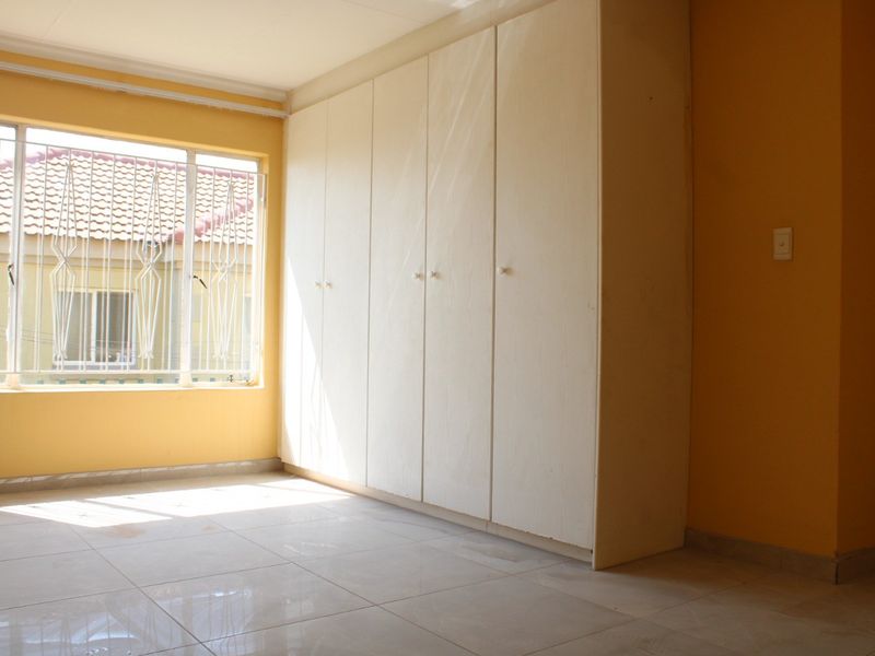 A vacant bedroom featuring built-in cupboards, tiled flooring, and a window fitted with security bars.