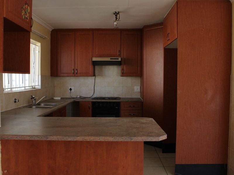 A functional kitchen featuring wood-look laminate cabinetry, a breakfast bar, built-in oven, hob, and extractor fan with tiled backsplash and flooring.