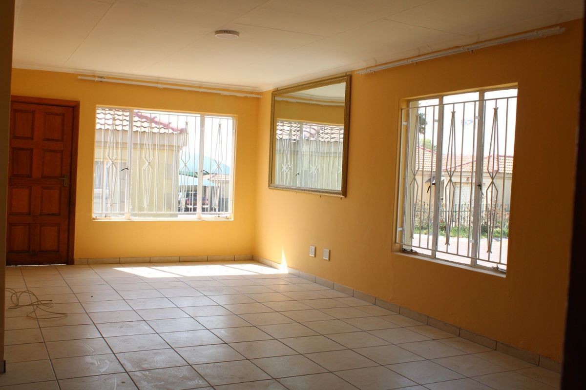 An empty, sunlit living room featuring tiled flooring, security bars on the windows, and a neutral wall finish, ready for personalization.