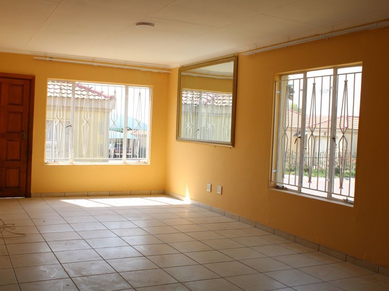 An empty, sunlit living room featuring tiled flooring, security bars on the windows, and a neutral wall finish, ready for personalization.