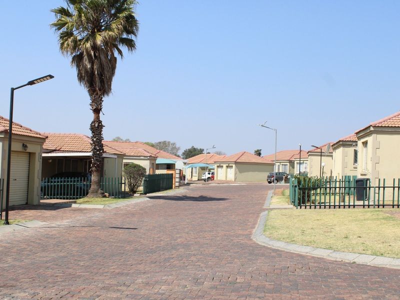 A view of a residential townhouse complex featuring paved driveways, tiled roof units, and perimeter metal fencing.