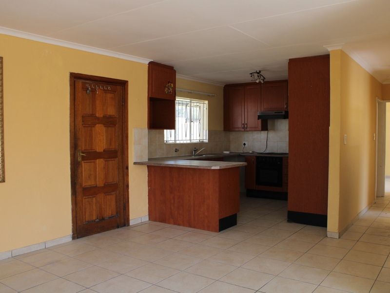 Open plan kitchen area featuring wooden cabinetry, laminate countertops, built-in oven, extractor fan, and tiled flooring, leading into an adjacent living space.