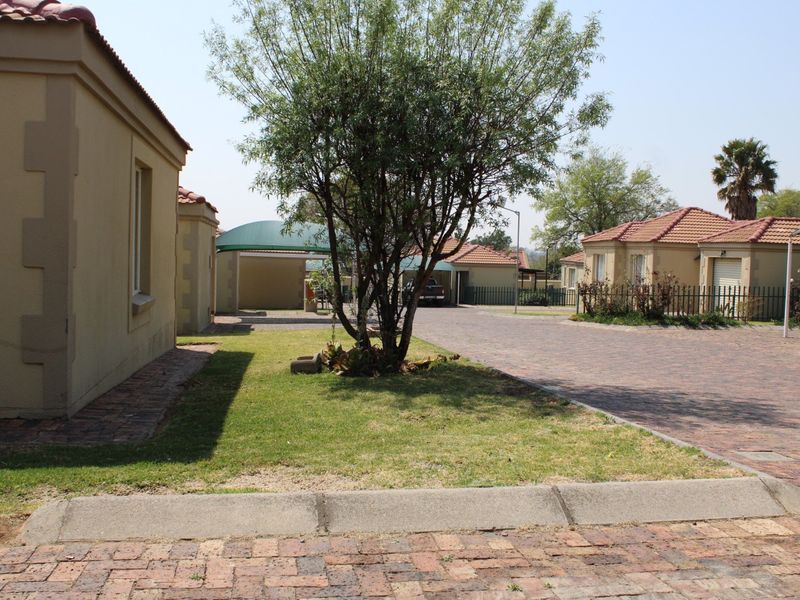 A view of the townhouse complex exterior featuring paved driveways, carports, and well-maintained garden areas with established trees.