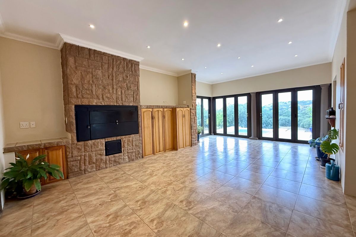Spacious living area featuring a prominent stone-clad fireplace, built-in cabinetry, tiled floors, and large stacker doors opening to an outdoor view.