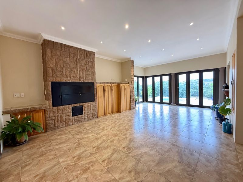 Spacious living area featuring a prominent stone-clad fireplace, built-in cabinetry, tiled floors, and large stacker doors opening to an outdoor view.