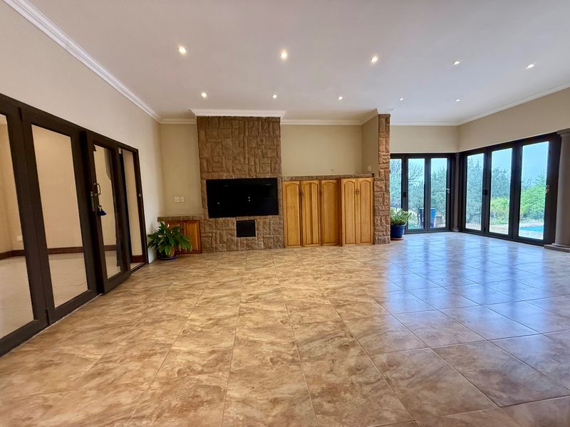 Spacious living area featuring tiled floors, a prominent stone-clad fireplace, built-in cabinetry, and large aluminium stacker doors providing access to the outdoor area.