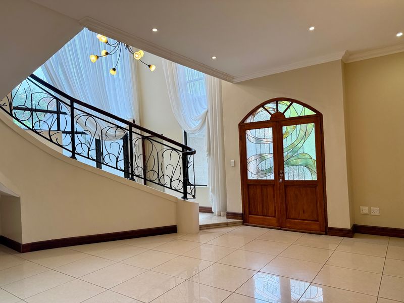 Spacious double-volume entrance hall featuring elegant wrought iron staircase railing, stained glass double doors, and polished porcelain floor tiles.