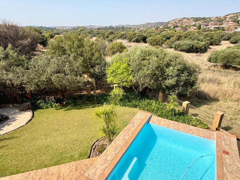 Elevated view of a private swimming pool with tiled coping, overlooking a well-maintained garden and expansive natural landscape.