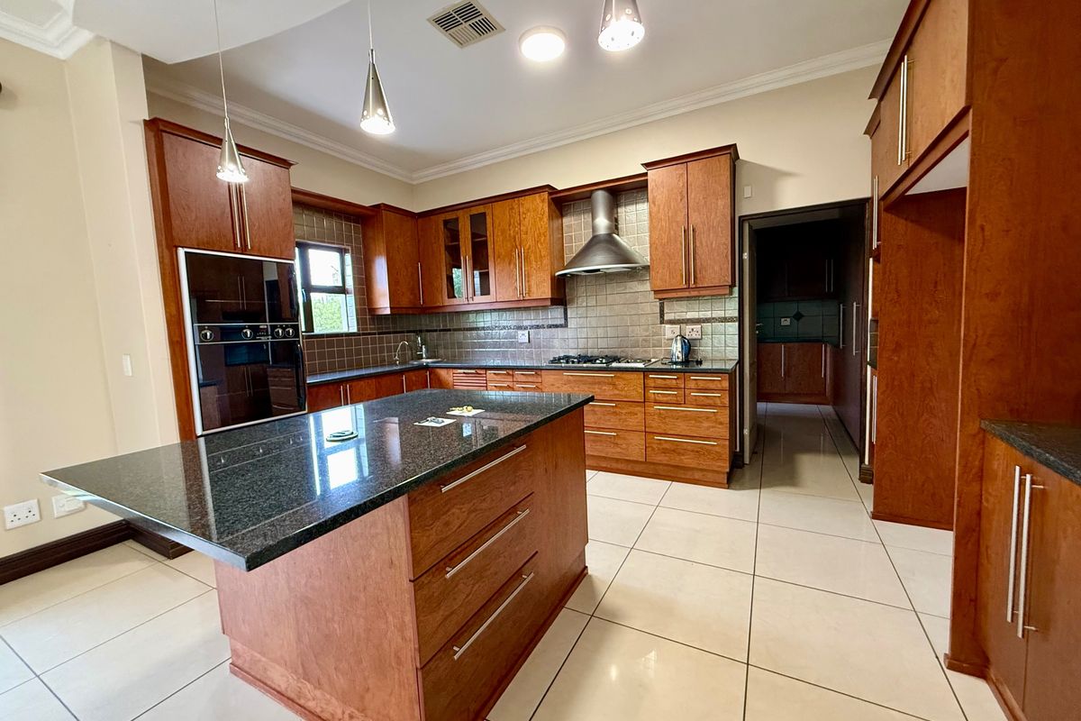 Spacious kitchen featuring wooden cabinetry, granite countertops, a central island, and built-in appliances, with direct access to a scullery area.