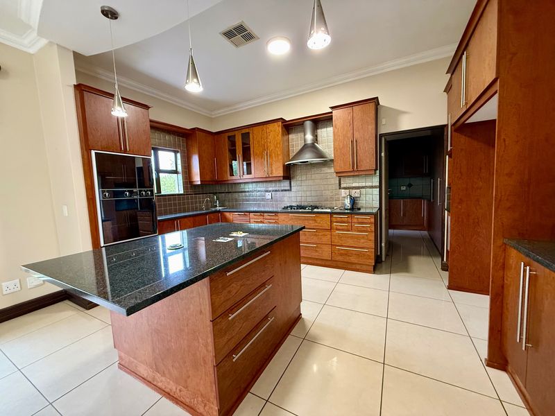 Spacious kitchen featuring wooden cabinetry, granite countertops, a central island, and built-in appliances, with direct access to a scullery area.