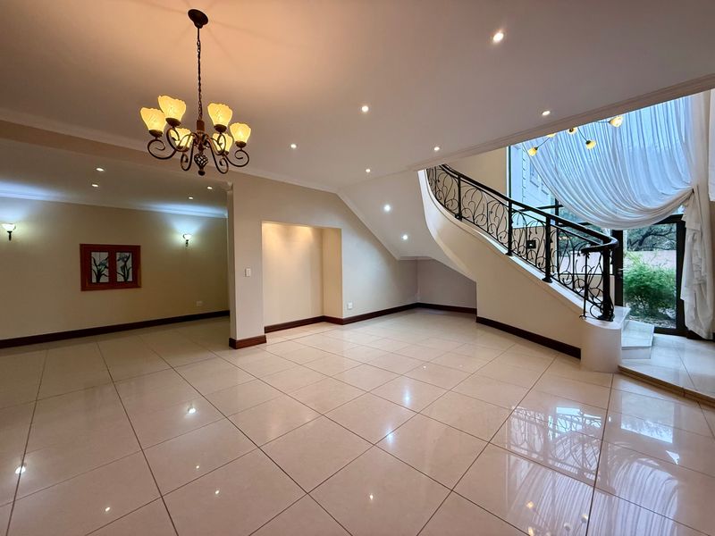 Spacious entrance hall featuring a grand curved staircase with wrought iron balustrade, polished tiled flooring, and recessed lighting.