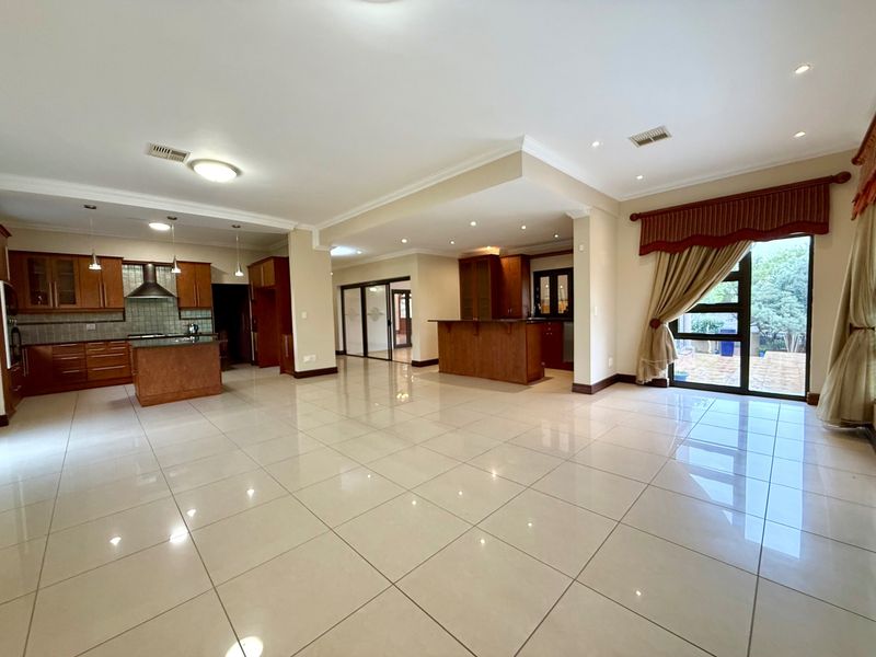 Spacious open-plan living and kitchen area featuring tiled flooring, wooden cabinetry, a central kitchen island, and direct access to the outdoor patio.