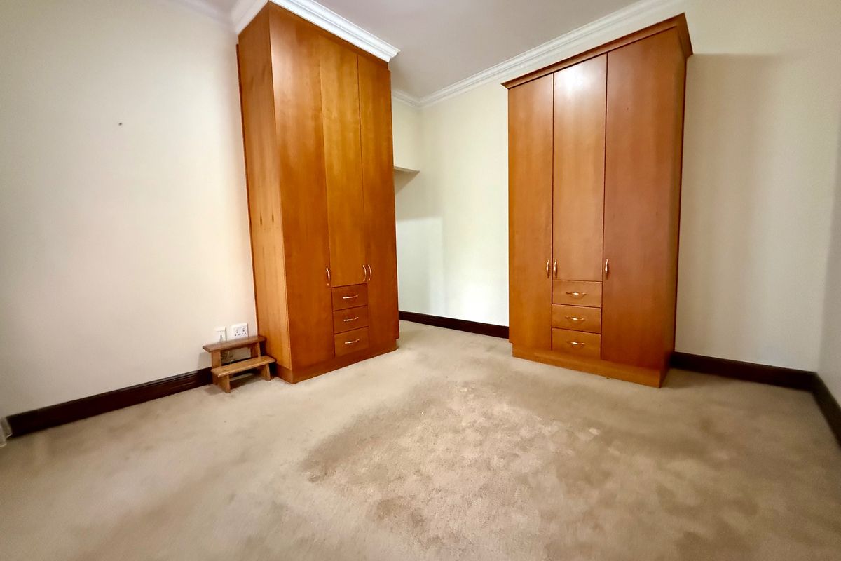 A spacious bedroom featuring built-in wooden cupboards, crown molding, and carpeted flooring, offering a blank canvas for personalization.