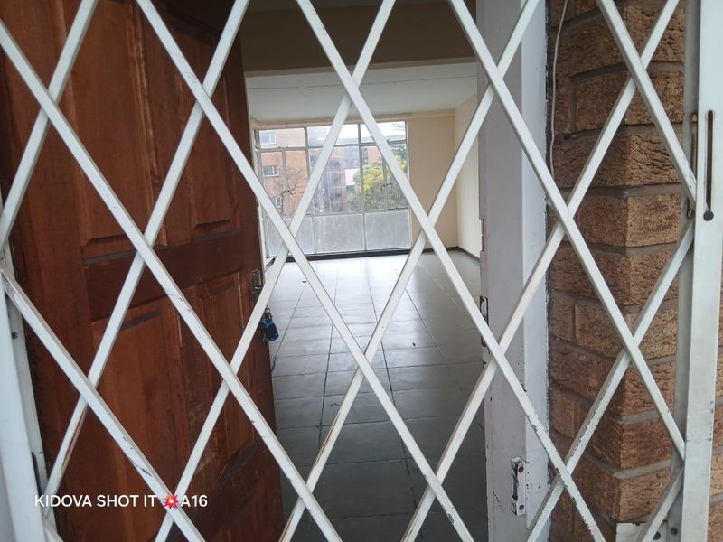 An empty, open-plan living area featuring tiled flooring and large windows, viewed through a security gate.
