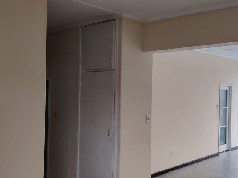An empty open-plan living area featuring tiled flooring, built-in storage cupboards, and access to an enclosed balcony with large windows.