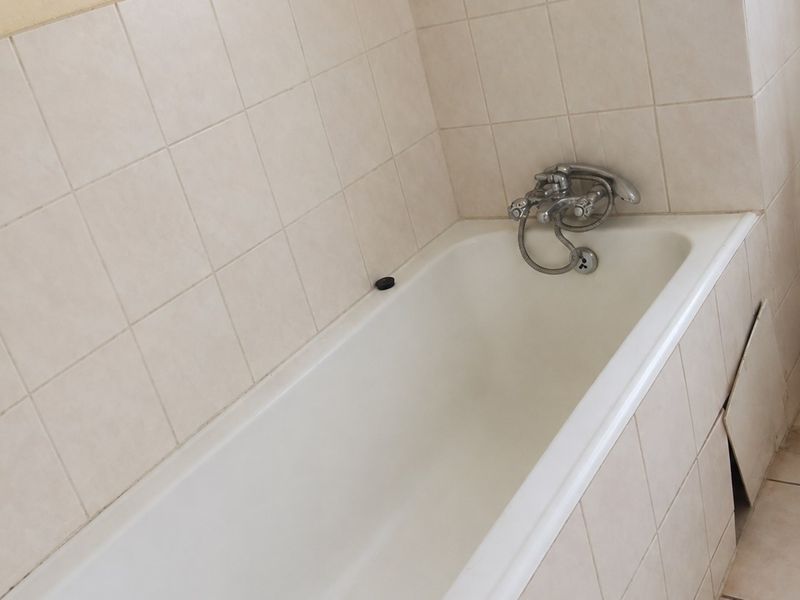 A functional bathroom featuring a standard bathtub with chrome mixer tap, finished with neutral ceramic wall and floor tiling.