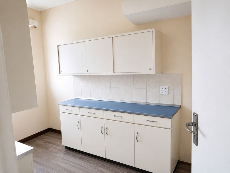 A clean, empty kitchen area featuring white cabinetry, a blue laminate countertop, tiled backsplash, and wood-look laminate flooring.