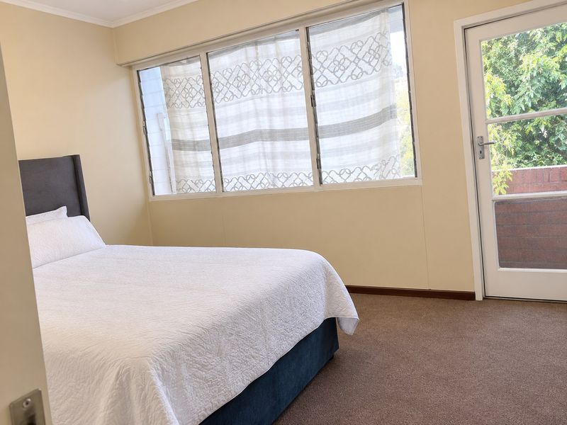 A well-lit bedroom featuring carpet flooring, large sliding windows, and direct access to an outdoor balcony area.
