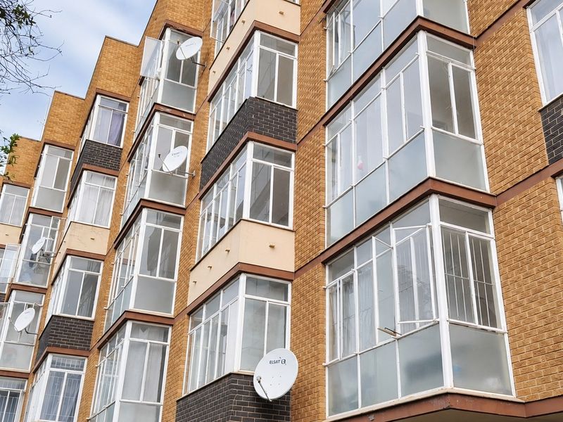 Exterior view of a multi-story apartment building featuring brick cladding and multiple enclosed balcony units with satellite dish installations.