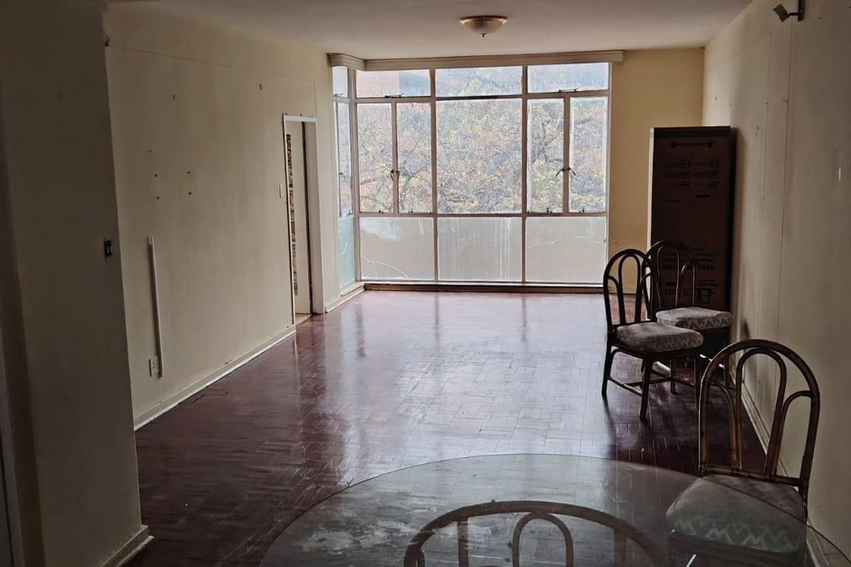 Spacious living area featuring original parquet flooring and large windows, offering a blank canvas for renovation and modernization.