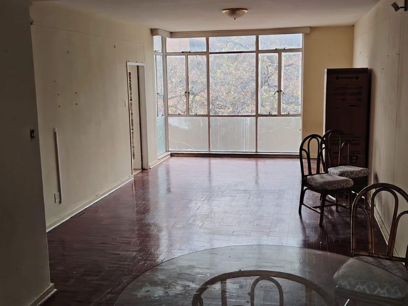 Spacious living area featuring original parquet flooring and large windows, offering a blank canvas for renovation and modernization.