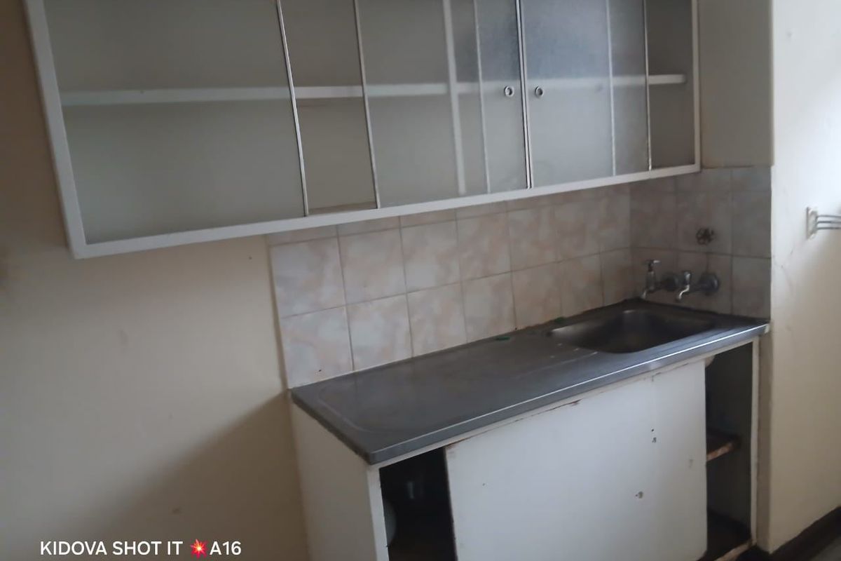 A dated kitchen area featuring a stainless steel sink, tiled splashback, and original wall-mounted and base cabinetry in need of renovation.