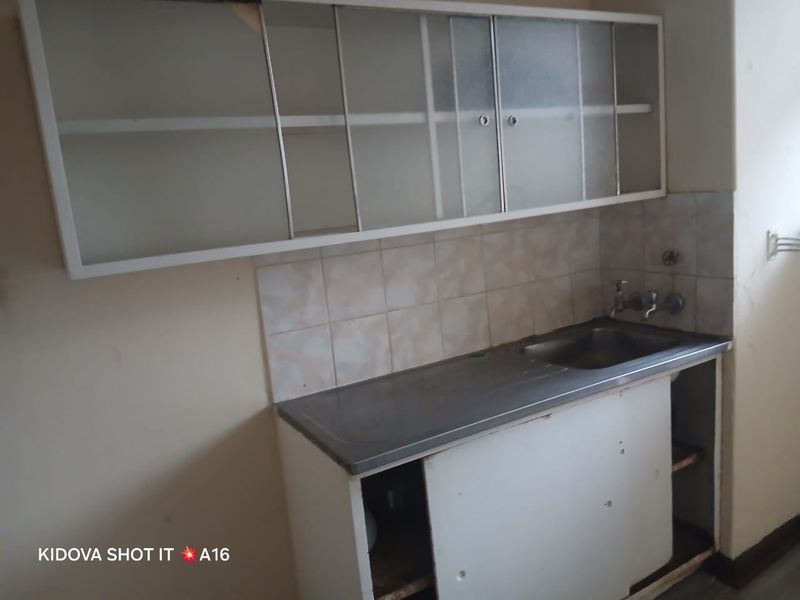 A dated kitchen area featuring a stainless steel sink, tiled splashback, and original wall-mounted and base cabinetry in need of renovation.