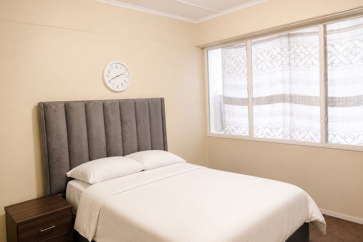 A well-lit bedroom featuring neutral wall tones, carpeted flooring, and a large window allowing for natural light.