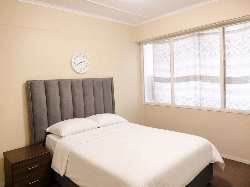 A well-lit bedroom featuring neutral wall tones, carpeted flooring, and a large window allowing for natural light.